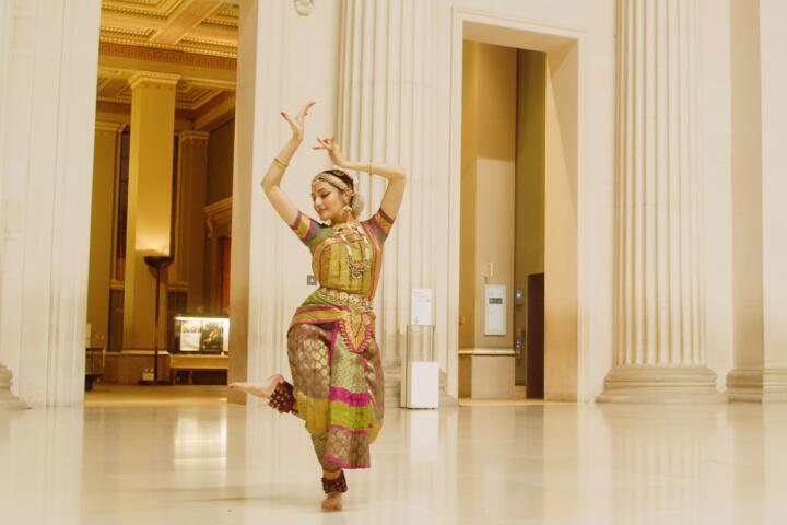 South Asian dancer in colourful clothes dancing in a white museum space